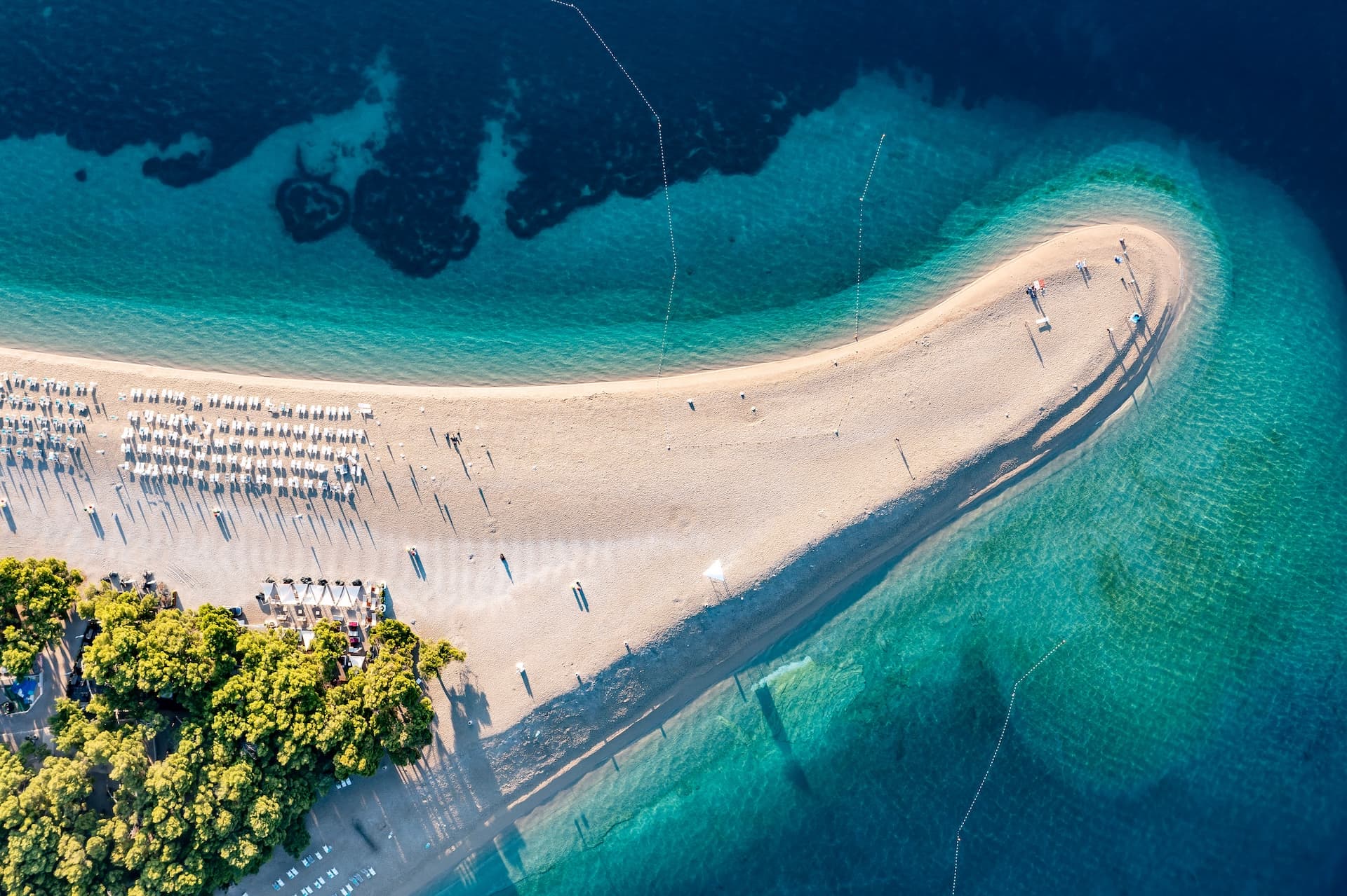 Aerial view of a distinctive white pebble beach spit surrounded by turquoise and deep blue sea water.