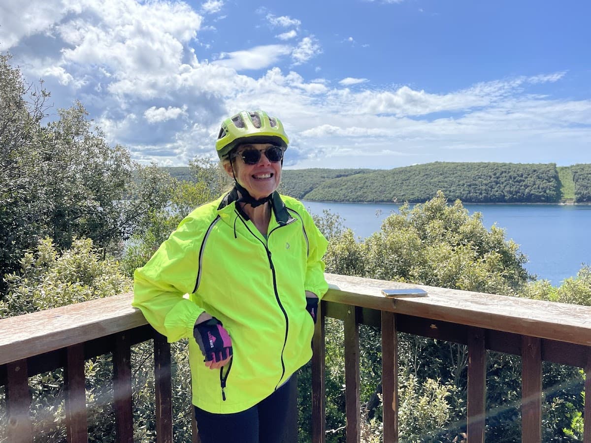 Cyclist in bright jacket smiling on wooden overlook above a large body of water.