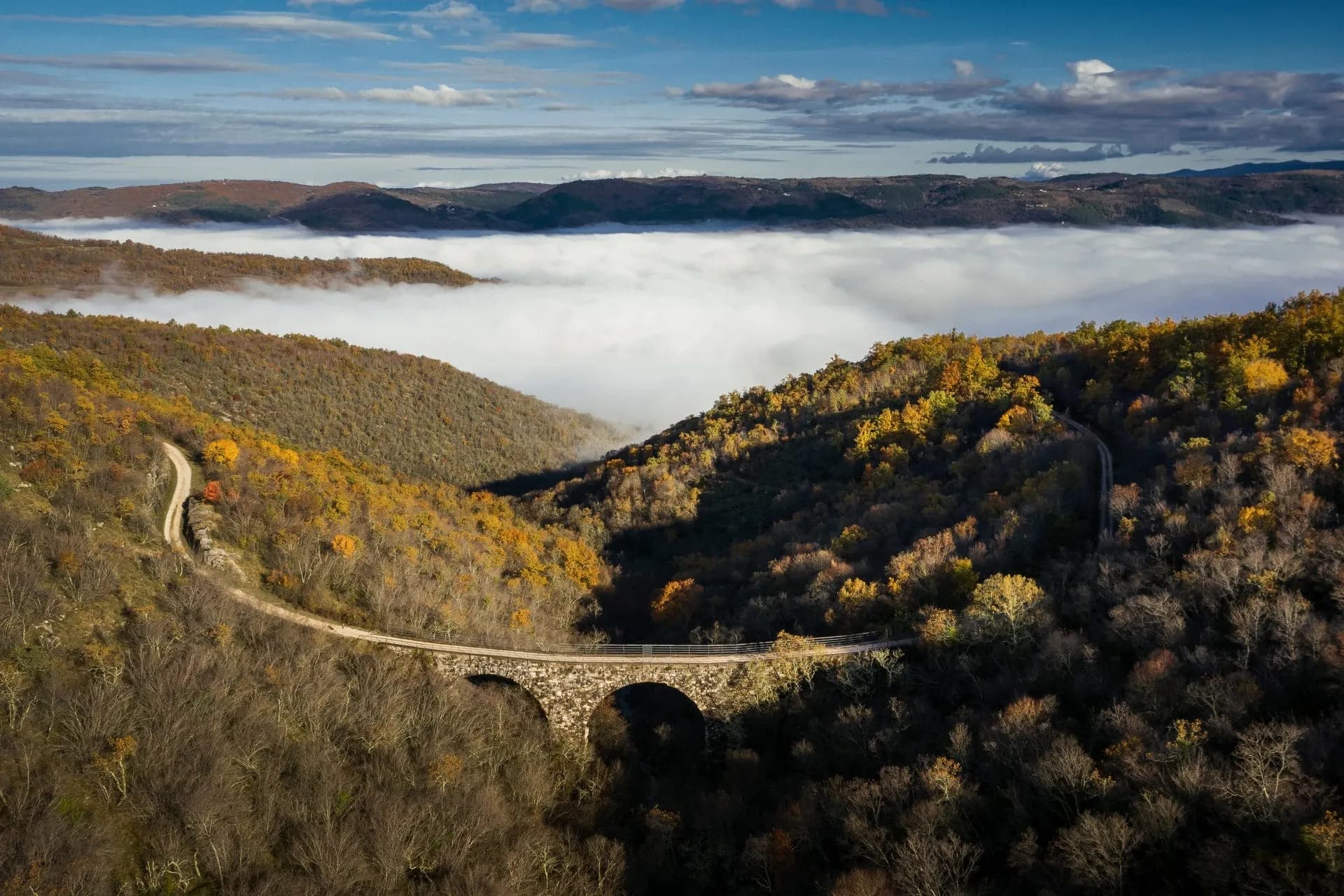 Stone arched former railroad bridge over forested valley with autumn colors and low cloud inversion