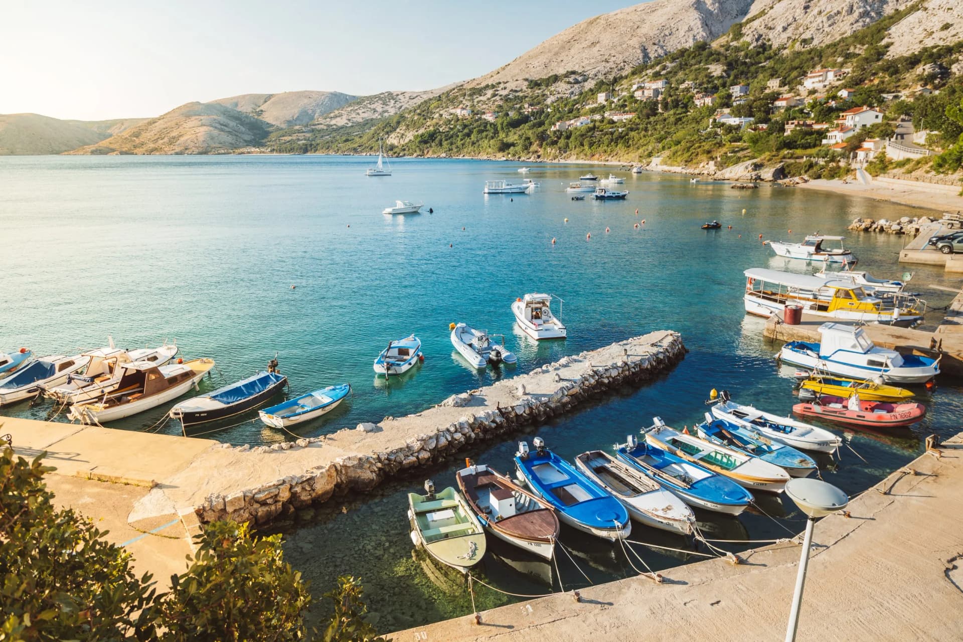 Blick auf den Hafen und die Bucht von Stara Baška, Kroatien mit vielen bunten Booten, dem türkisblauen Meer und Bergen