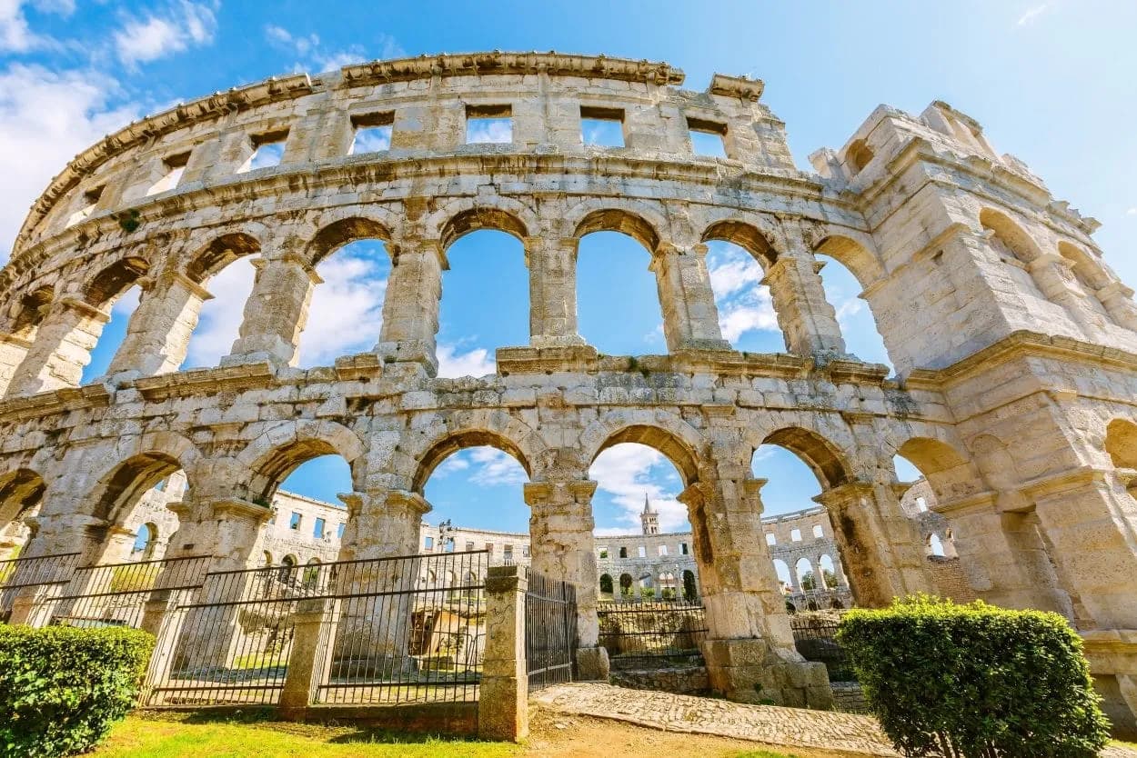 Roman amphitheater ruins with arches against a bright blue sky in Pula.