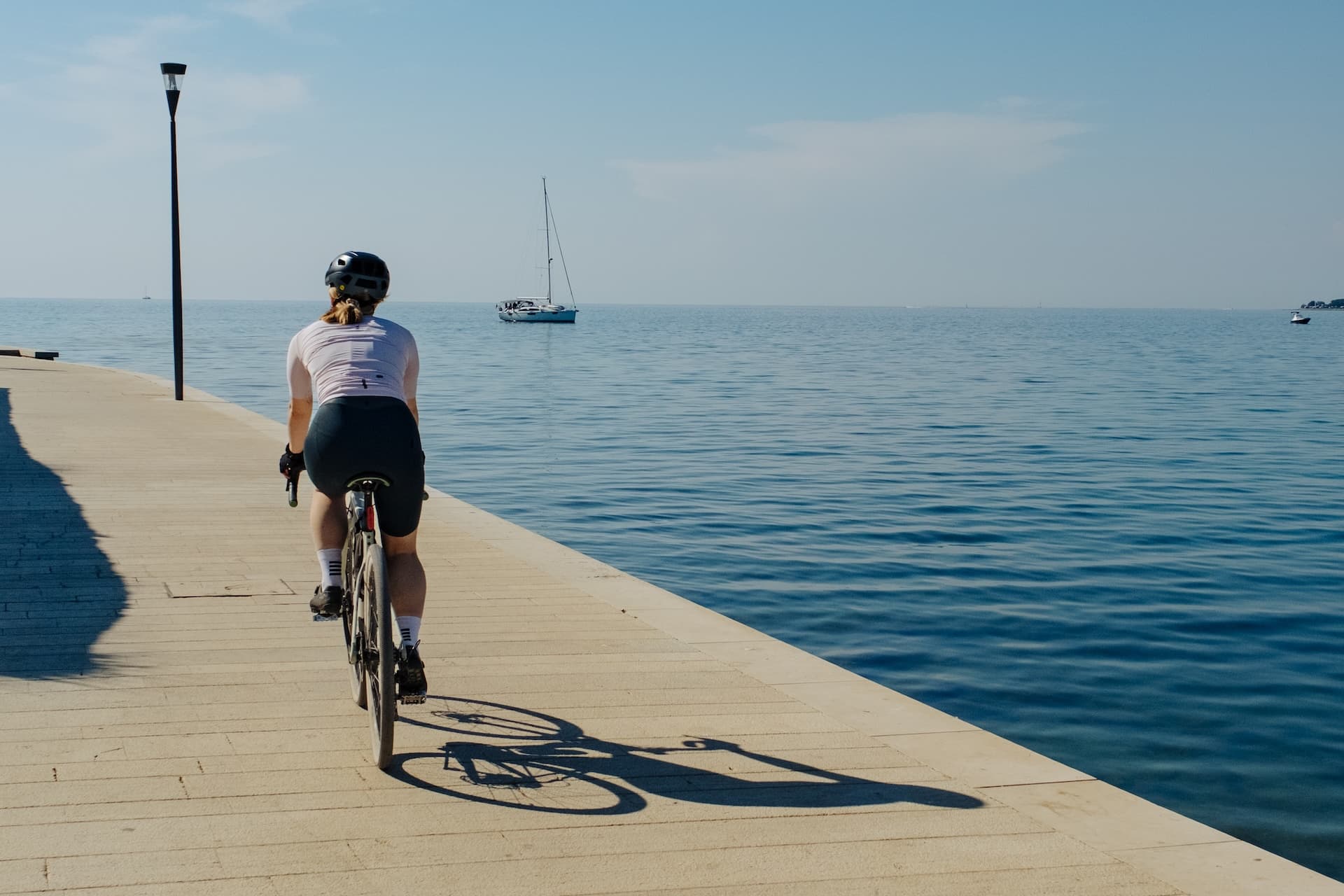 Cyclist riding along a stone promenade next to the blue Adriatic Sea with a sailboat.