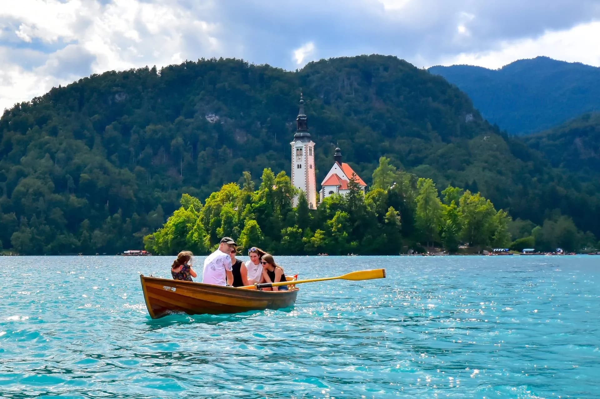 Rowing boat on Lake Bled with island church and forested mountains in Slovenia.