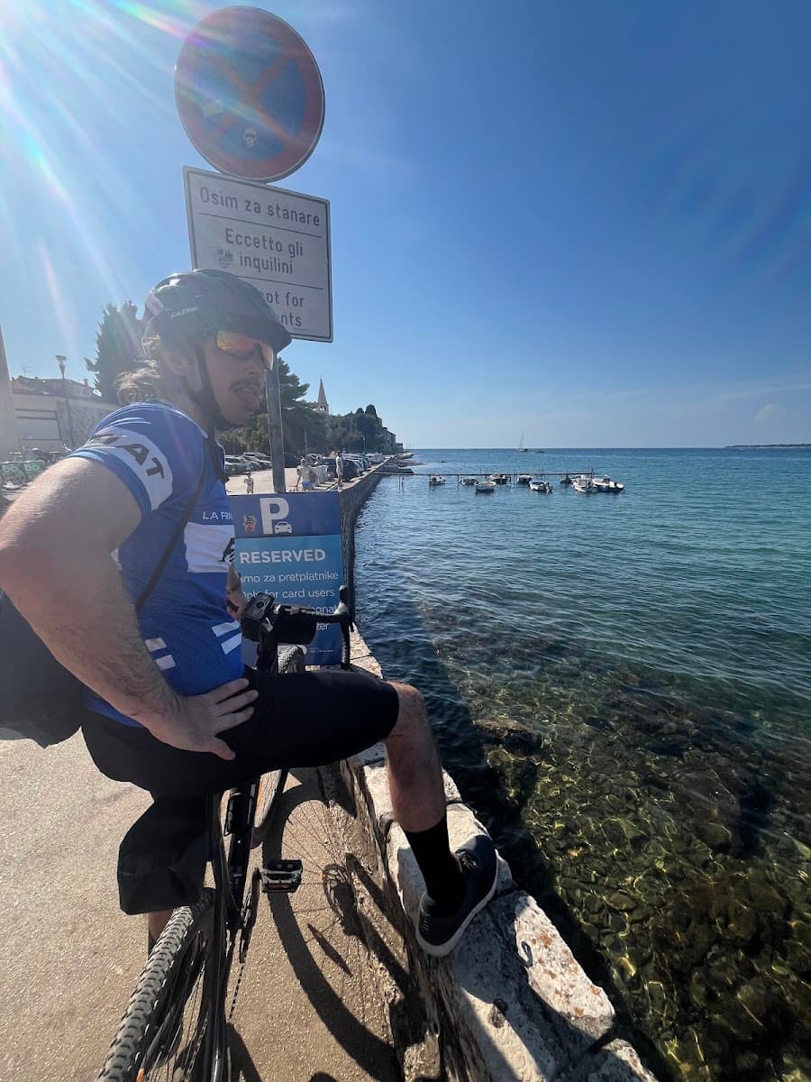 Cyclist resting by the sea with small boats docked along the rocky coast