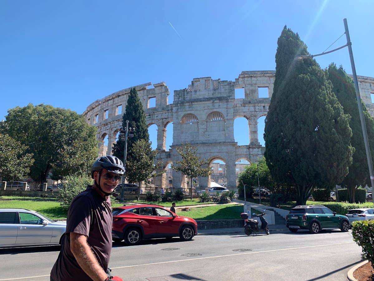 Cyclist with helmet in front of ancient Roman amphitheater and parked cars
