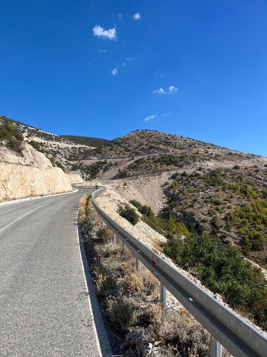 Winding asphalt road climbing a barren mountain slope under a blue sky
