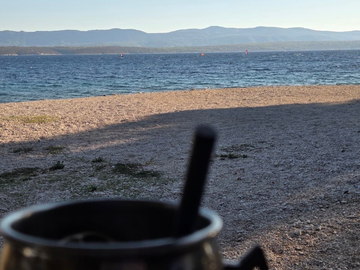 Pebble beach with blue sea and distant mountains viewed past a foreground container
