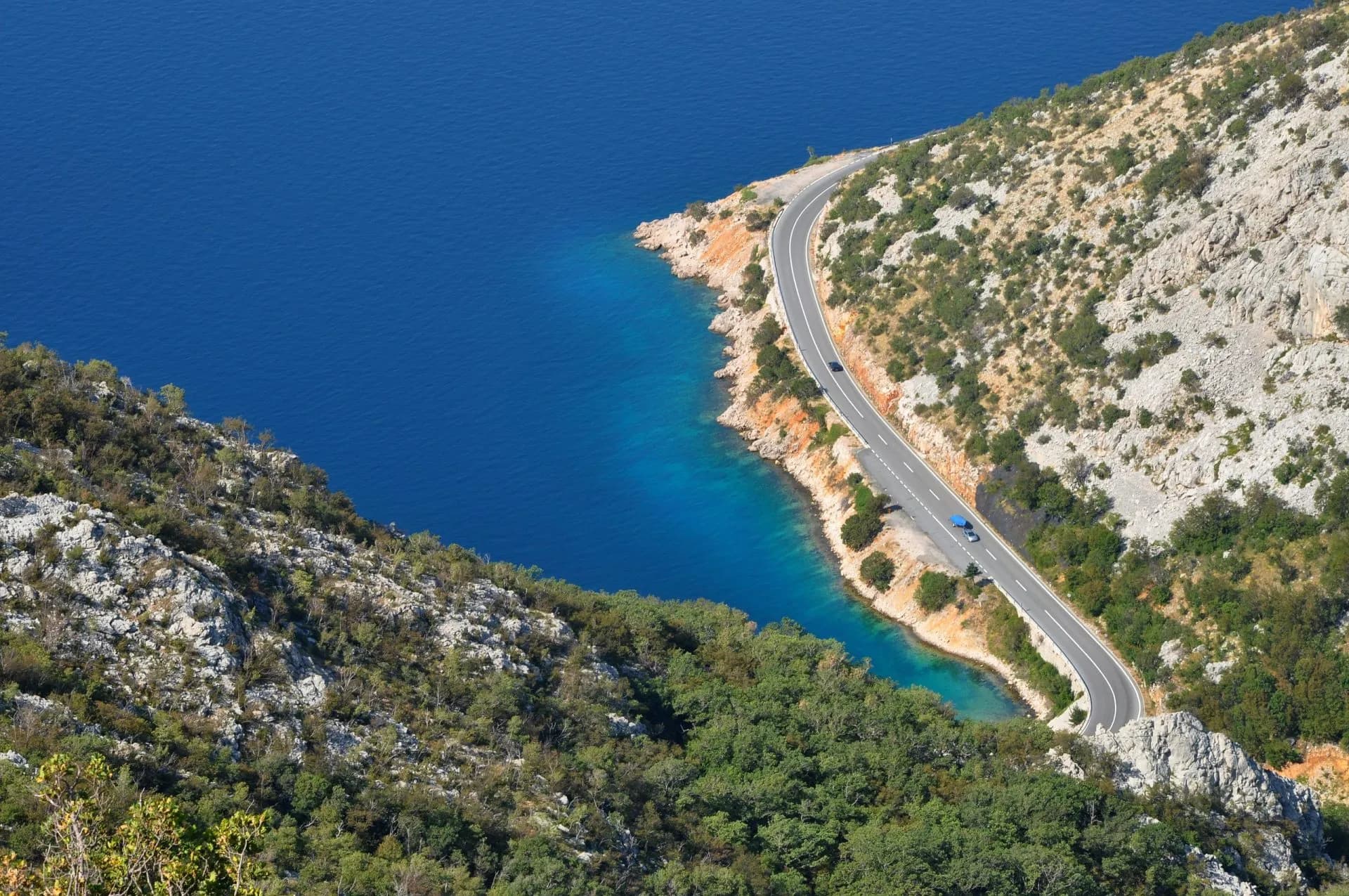 Winding coastal road hugging steep hillsides above bright blue Mediterranean sea in Croatia