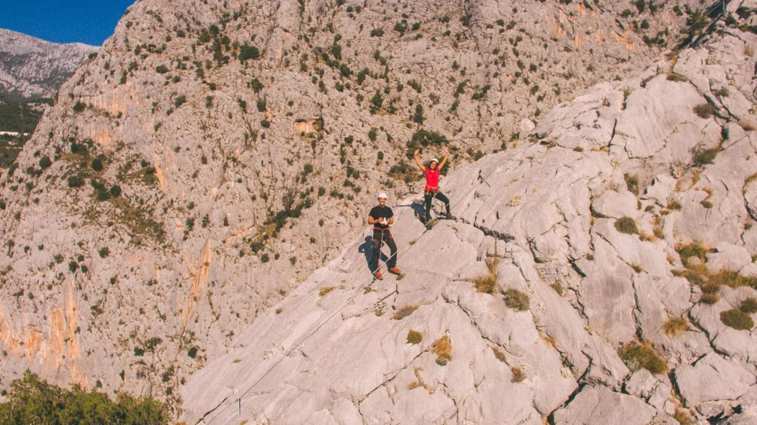 Via ferrata climbers on steep, rocky mountainside under clear blue sky