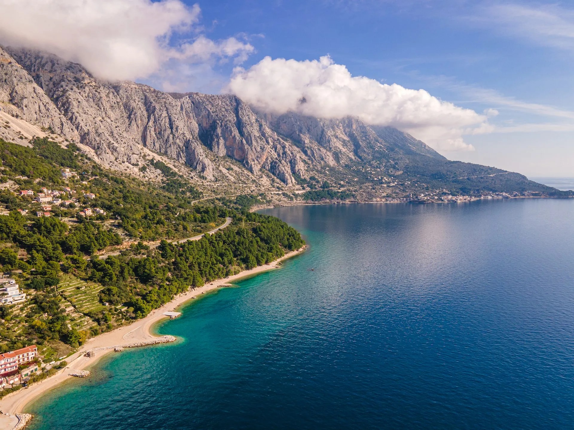 Coastal view of Biokovo mountains meeting turquoise sea, with small town and road.