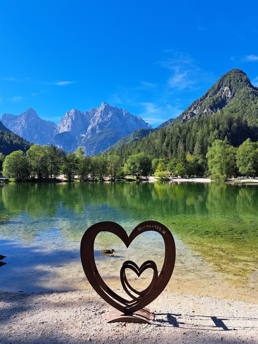 Metal heart sculpture by clear green lake with duck, backed by forested mountains