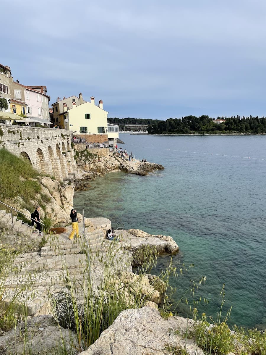 Coastal town with stone steps leading to turquoise sea, historic buildings on cliff