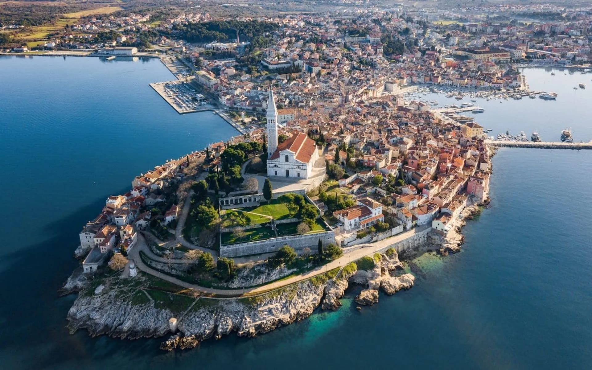 Aerial panorama of Rovinj peninsula town with white church tower overlooking the deep blue Adriatic Sea.