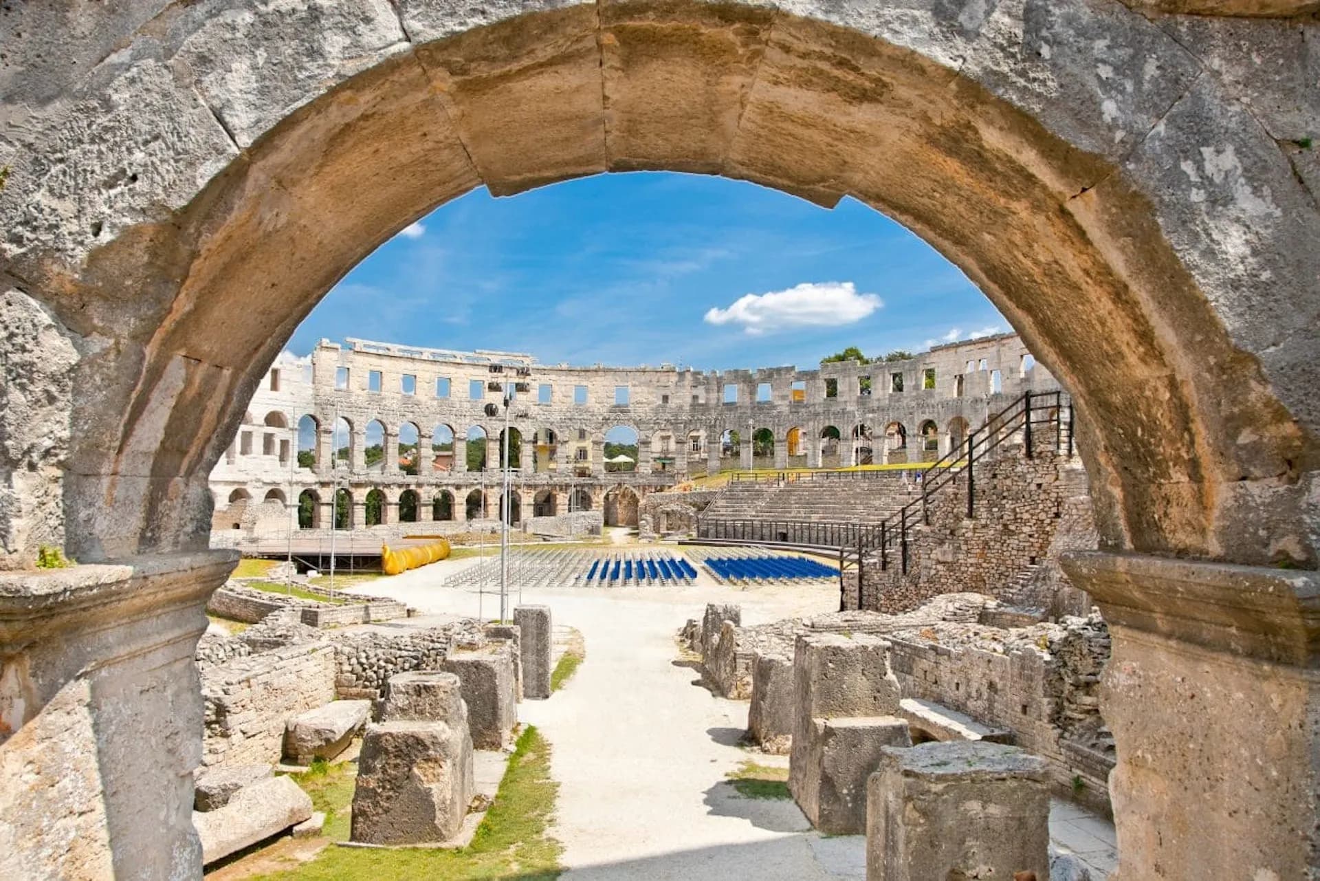 Ancient stone amphitheater entrance arch framing arena seating under a blue sky in Pula.