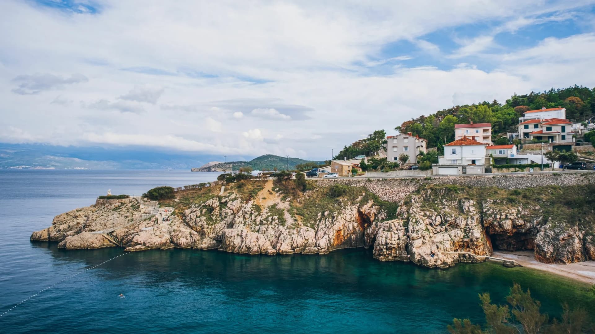 Image of a rocky coastline of island Krk with several building surrounded with trees in Vrbnik