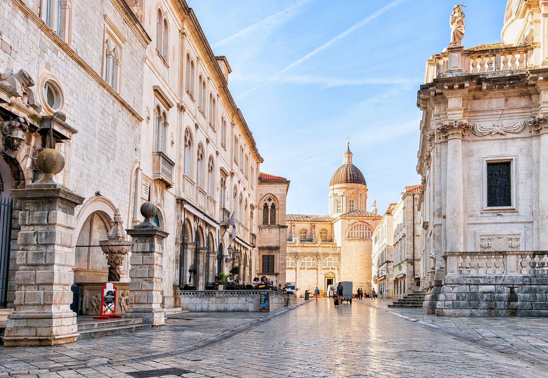 People walking on cobblestone street toward Dubrovnik Cathedral dome in Old City.