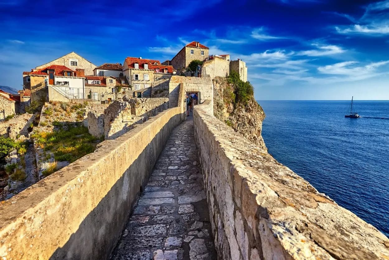 Stone walkway on Walls of Dubrovnik overlooking the Adriatic Sea with a sailboat.