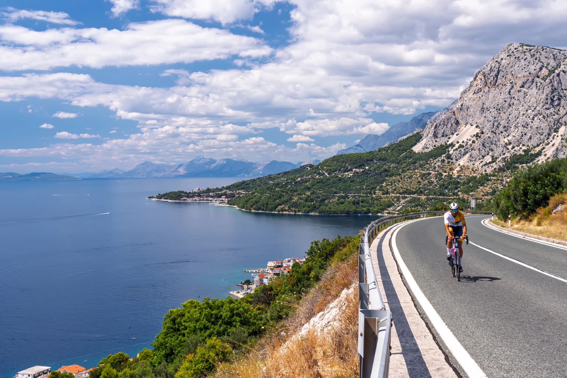 Capturing the essence of a perfect active vacation: a cyclist pedaling along a high-altitude road with incredible, expansive views of the sparkling sea and picturesque shoreline.Active Holiday