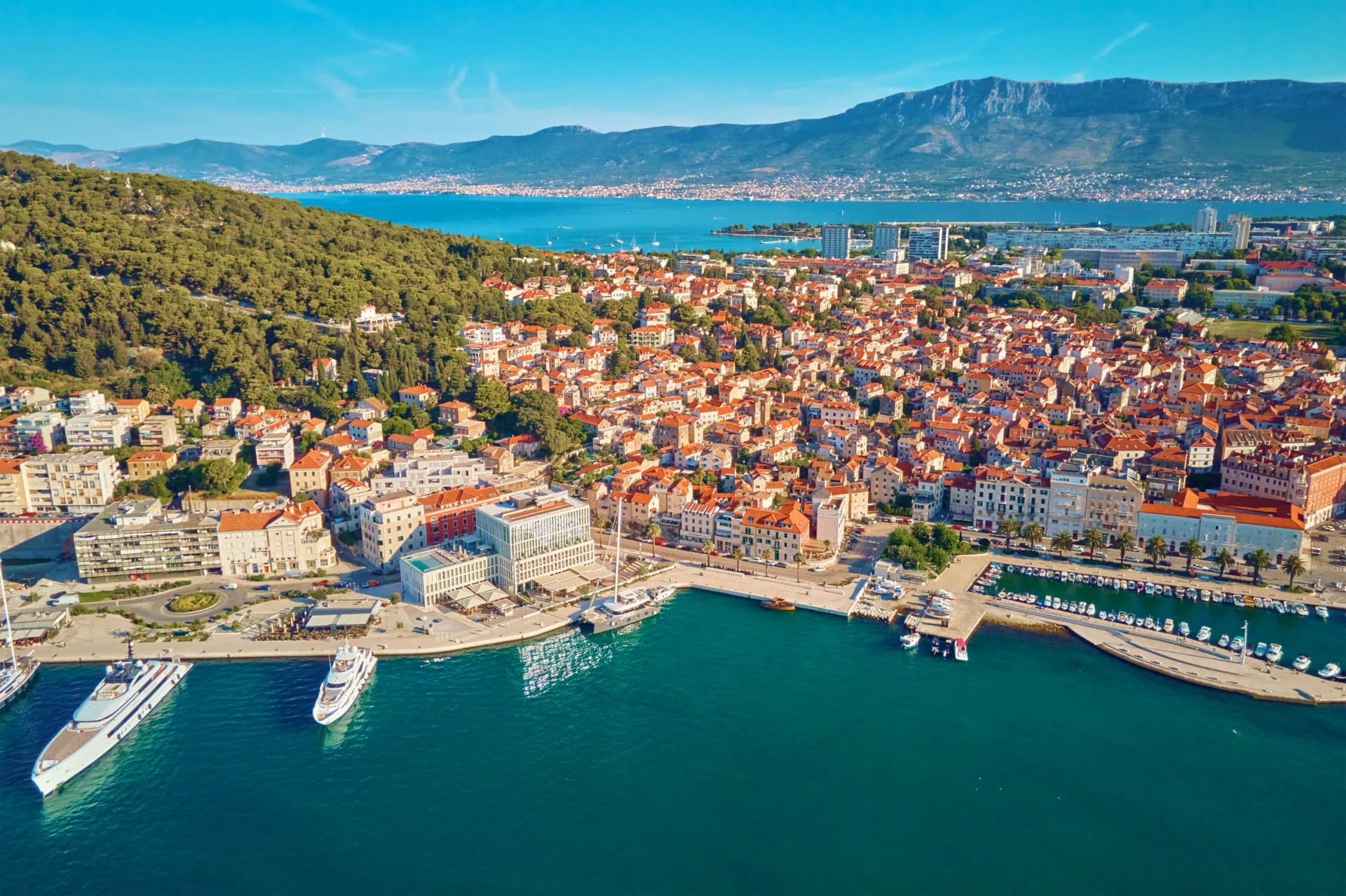Aerial view of Split, Croatia. Cityscape of coastal touristic city with harbor with mountains in background. Old town with historical red roof tiled buildings near Adriatic Sea