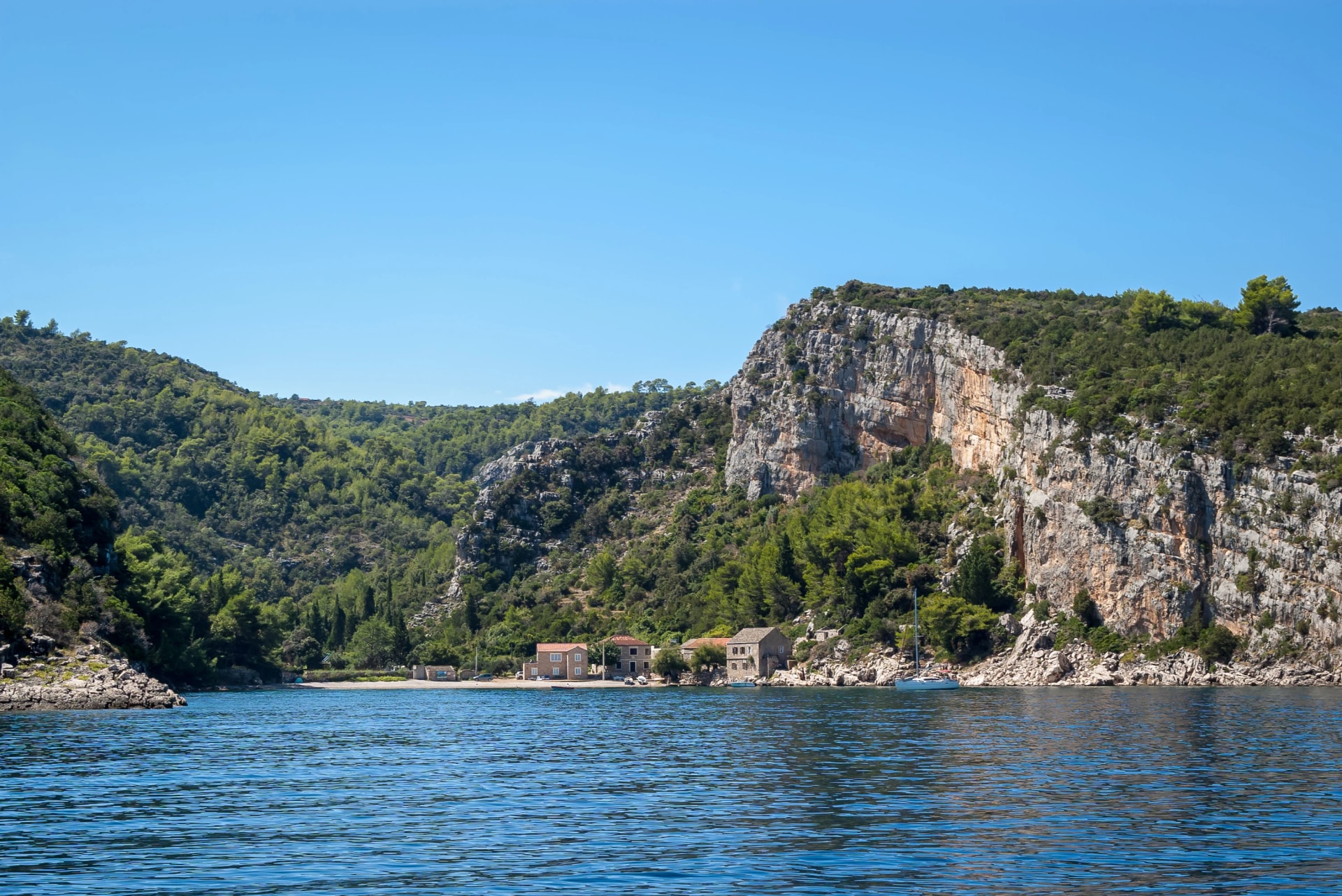 Beautiful small bay with several traditional stone houses, turquoise blue waters and a moored yacht, Pokrivenik bay, Island of Hvar, Croatia.