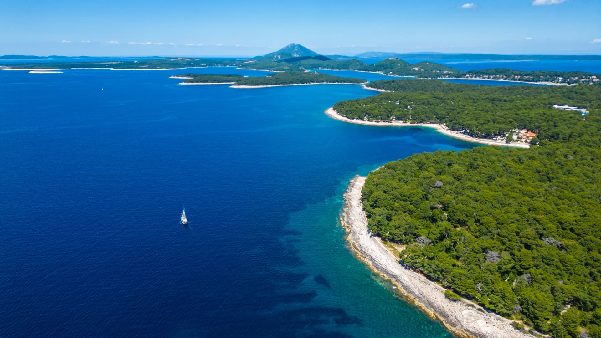 Aerial view of Camping Čikat on Lošinj (Losinj) island, surrounded by a beautiful pine forest and the Adriatic Sea. Known for XTERRA races, biking trails, and crystal-clear coastline views