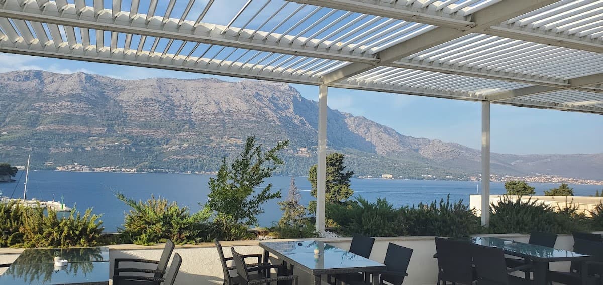 Outdoor terrace dining area with tables and chairs overlooking coastal waters and mountains