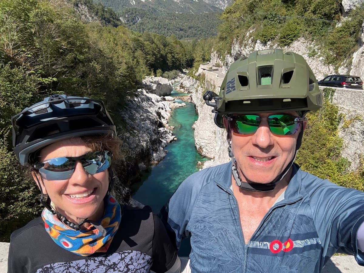 Cyclists taking a selfie with helmets and sunglasses overlooking a turquoise river gorge in a mountainous valley