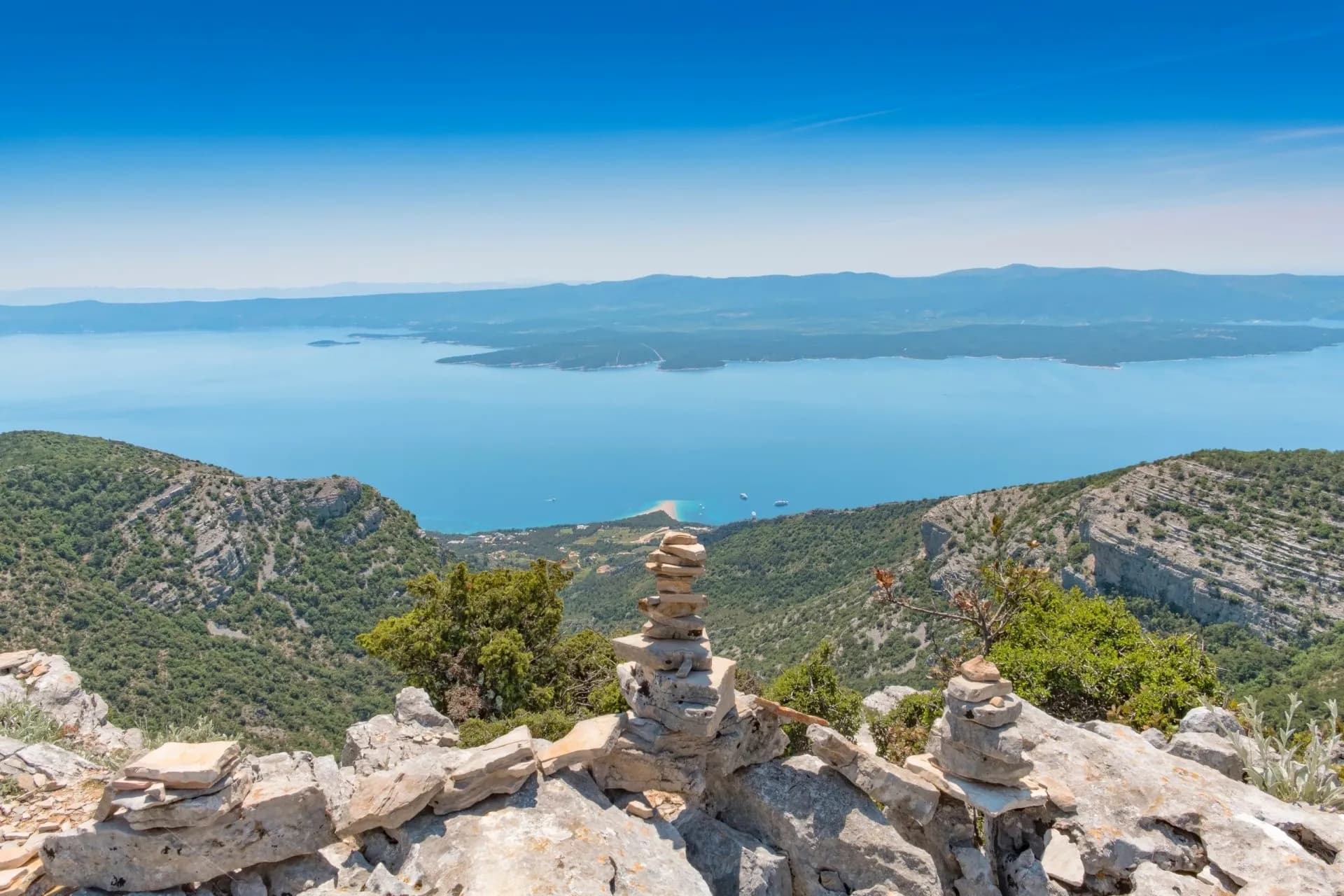 View from Vidova Gora showing stacked rocks overlooking forested slopes and blue sea.