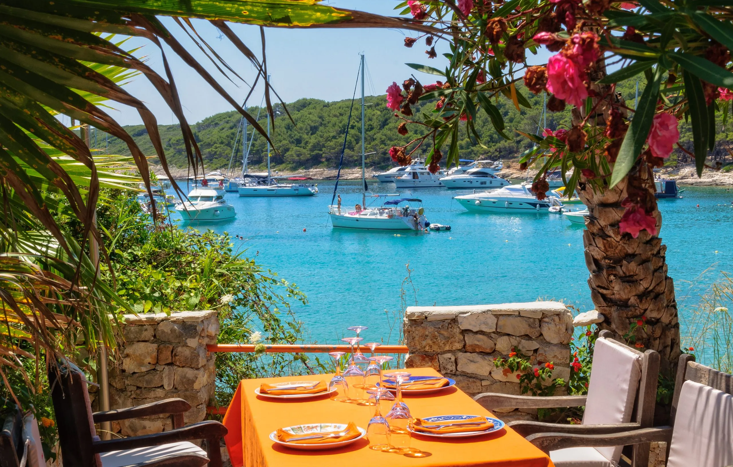 Voor anker liggende jachten in Milne Bay gefotografeerd vanaf het terras van een restaurant - Hvar, Kroatië